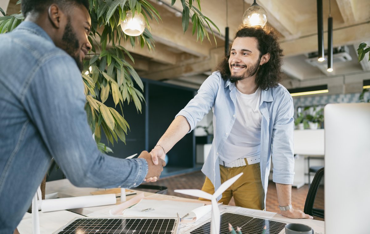 Two colleagues shaking hands over a desk of renewable energy models and plans