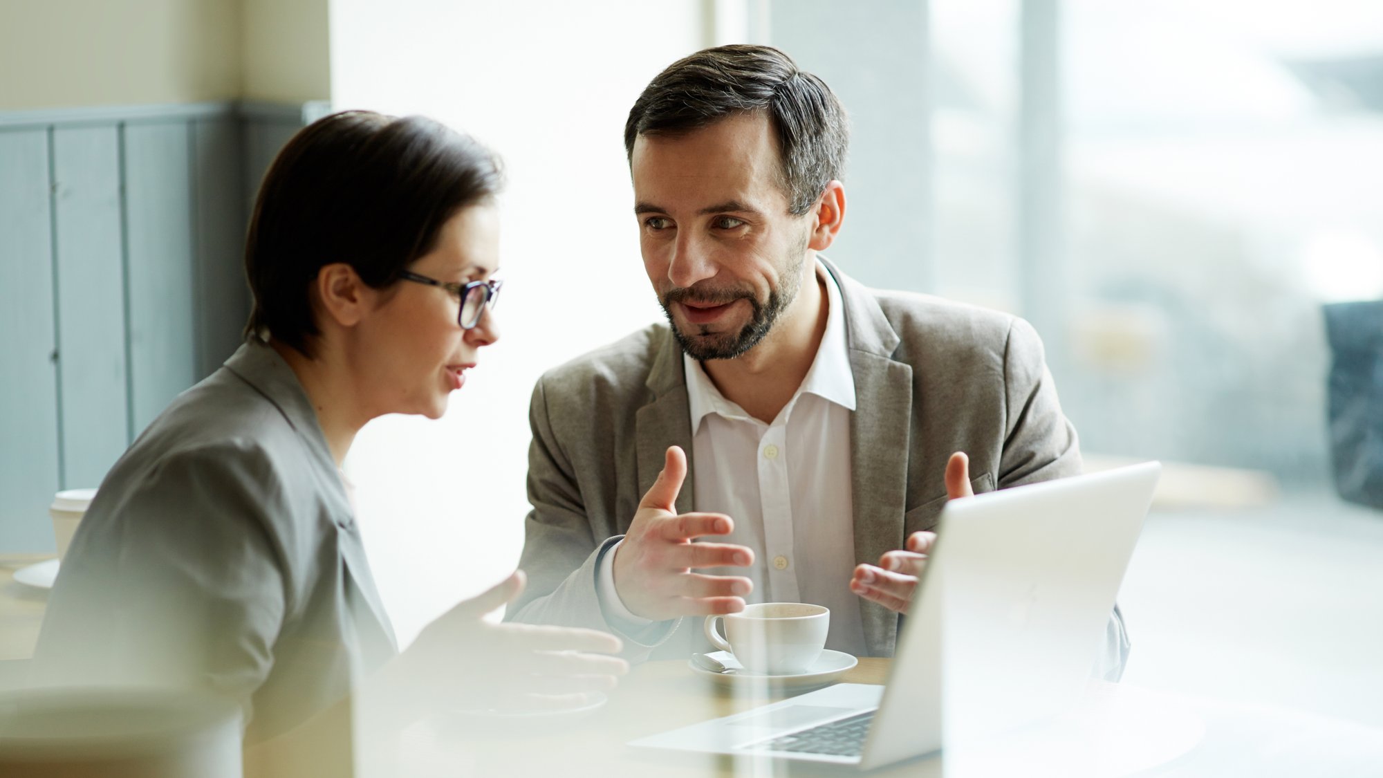 Two colleagues in conversation over a laptop at a bright office table