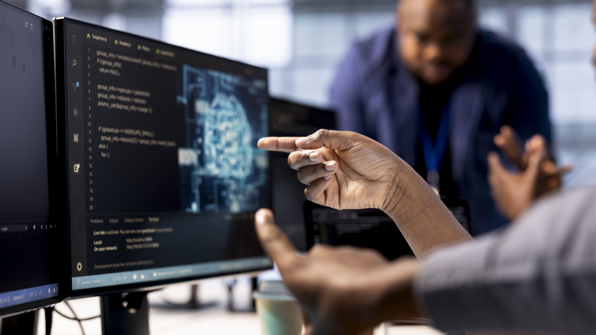 A developer pointing at code and an AI visualization on a monitor while a colleague looks on