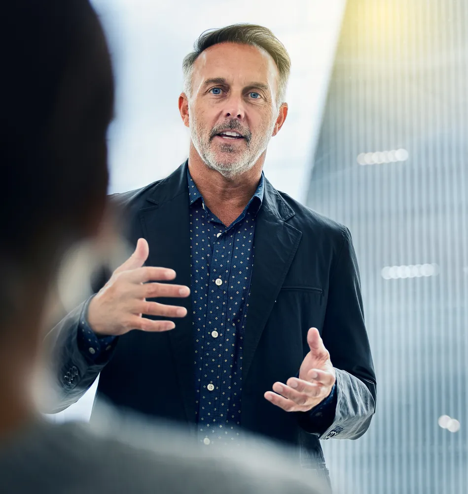An advisor in a navy blazer explaining something to a client in a bright office