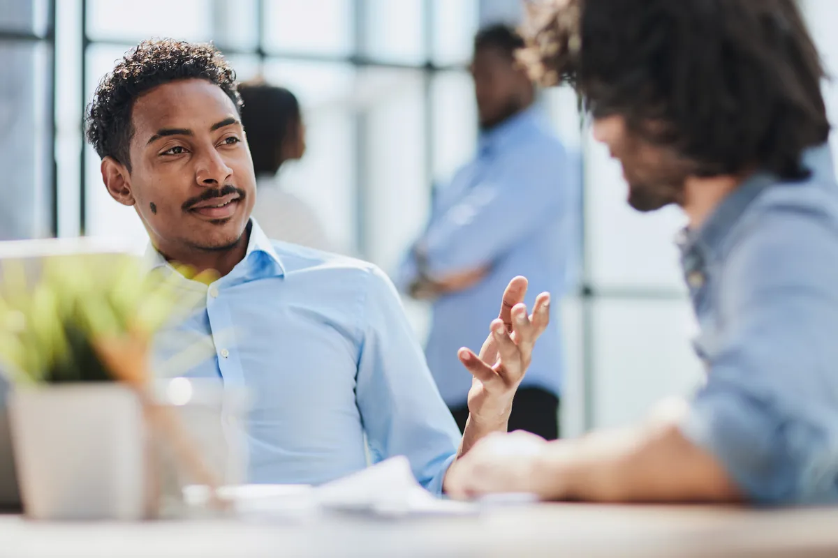 Two colleagues in conversation across a desk in a bright office