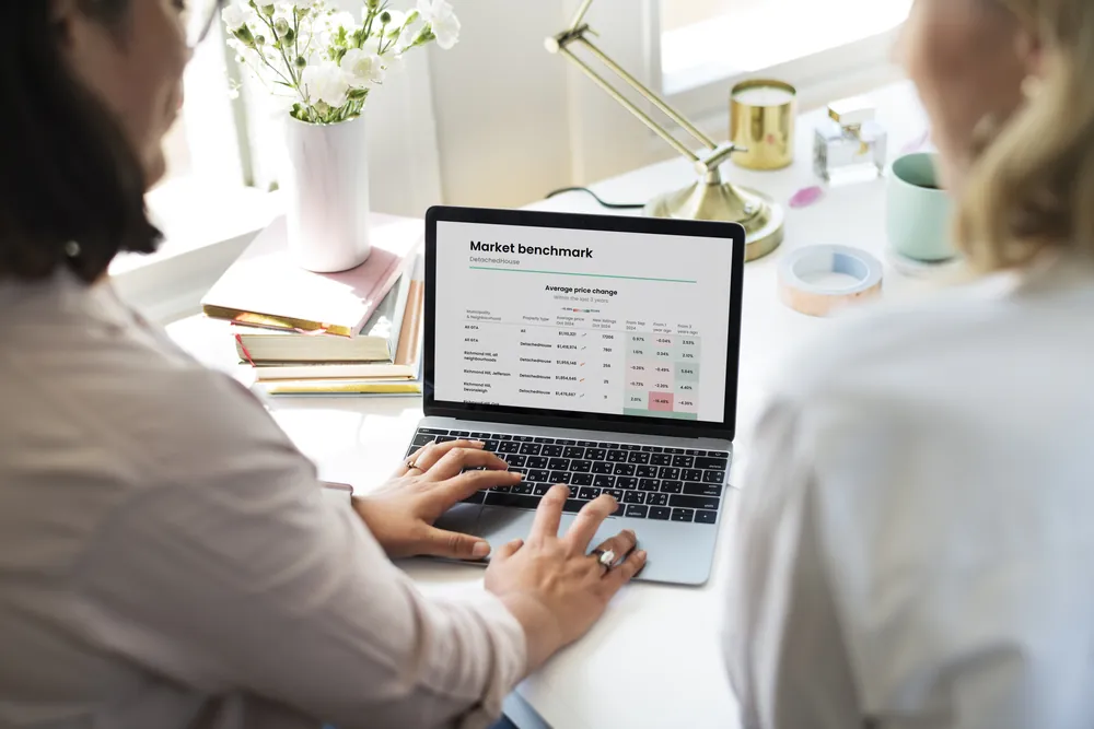 Two people reviewing a market benchmark report on a laptop